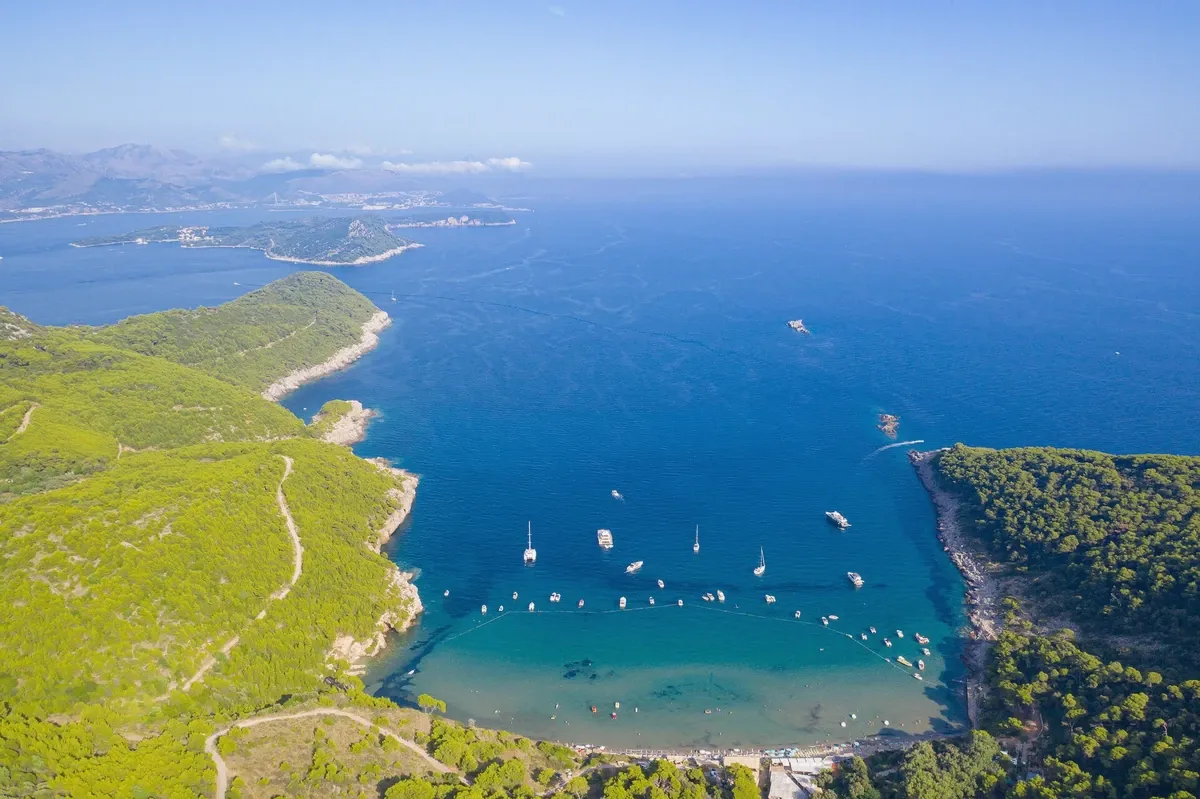 Aerial view of a green Adriatic island with boats at anchor in turquoise water, the quiet-side scenery of the Korcula boat adventure tour